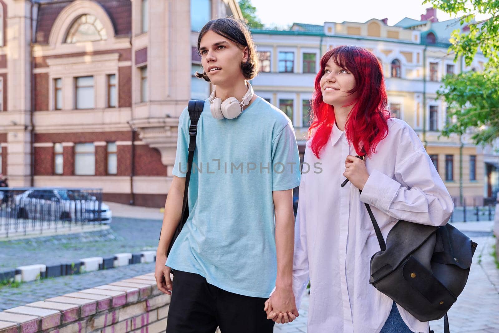 Couple of happy teenage friends walking holding hands, outdoor, on city street. Friendship, romantic, youth, leisure, relationship, lifestyle concept