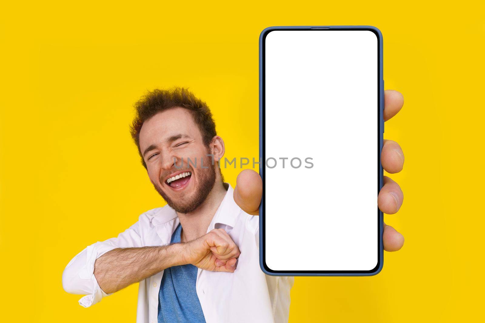 Yeah, chest hit happy excited young man with smartphone showing a white empty screen isolated over yellow game, bet, lottery win. Product placement. Mobile app advertisement.