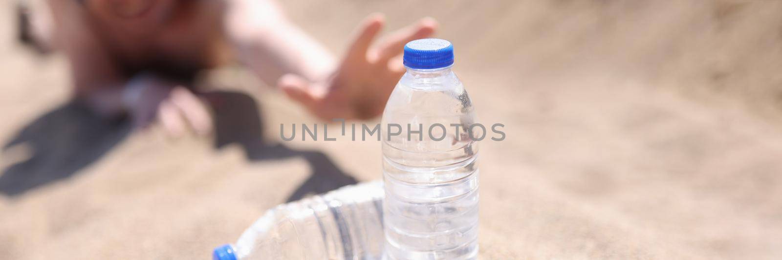 A man in the desert stretches on the sand for bottles of water by kuprevich