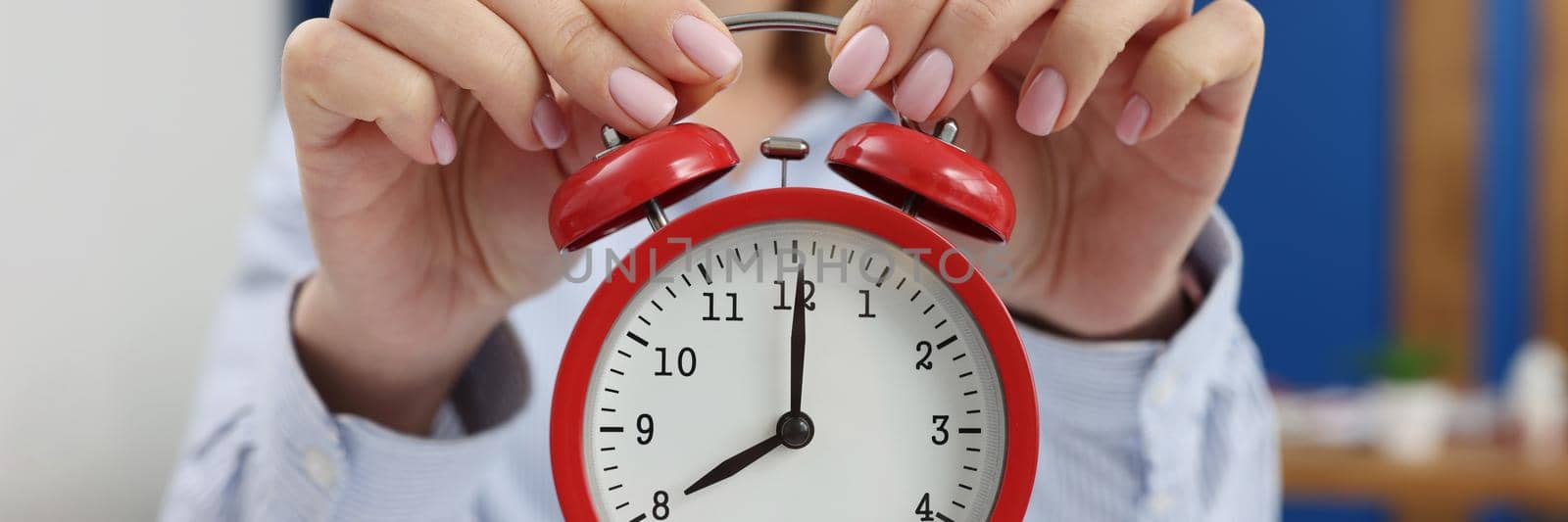 Woman holding a red alarm clock, close-up, blurry. Concept of day planning, meeting deadlines, productive morning