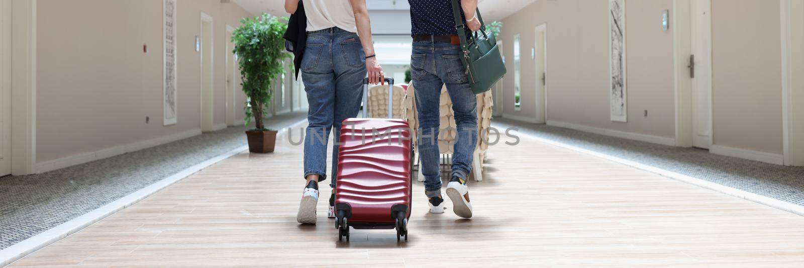 A man and a woman are walking with luggage along the hotel corridor, close-up, rear view. Accommodation in a resort complex