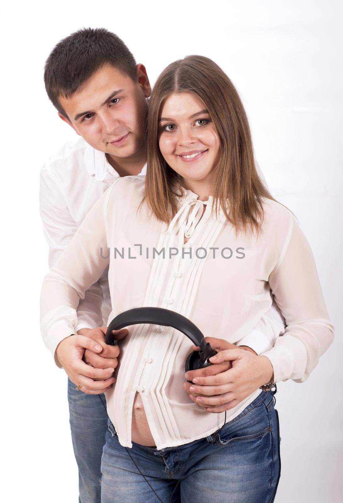 Pregnant woman and man in white shirts and jeans with headphones on white background