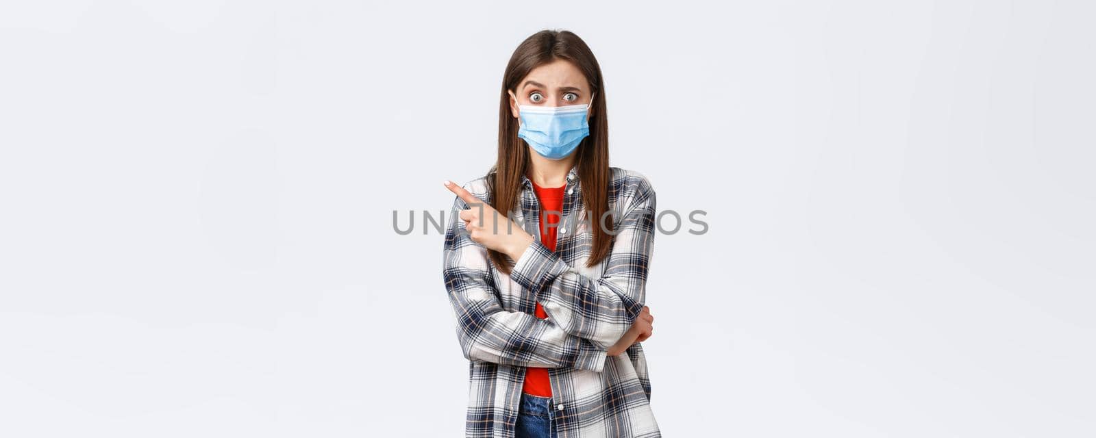 Coronavirus outbreak, leisure on quarantine, social distancing and emotions concept. Confused and worried girl asking question about smth strange, pointing finger left, wear medical mask covid-19.