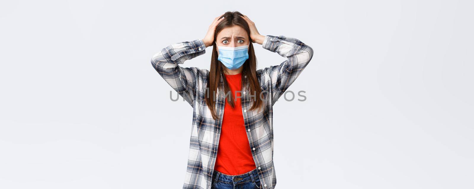 Different emotions, covid-19 pandemic, coronavirus self-quarantine and social distancing concept. Alarmed and worried, panicking young woman in medical mask, grab head indecisive, feel scared.