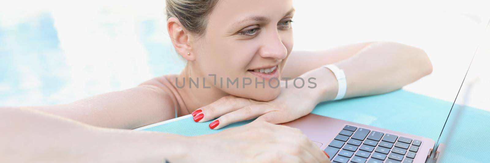 Young woman in the pool uses a laptop, close-up. Freelancer on vacation, luxury resort. Remote work, tourism