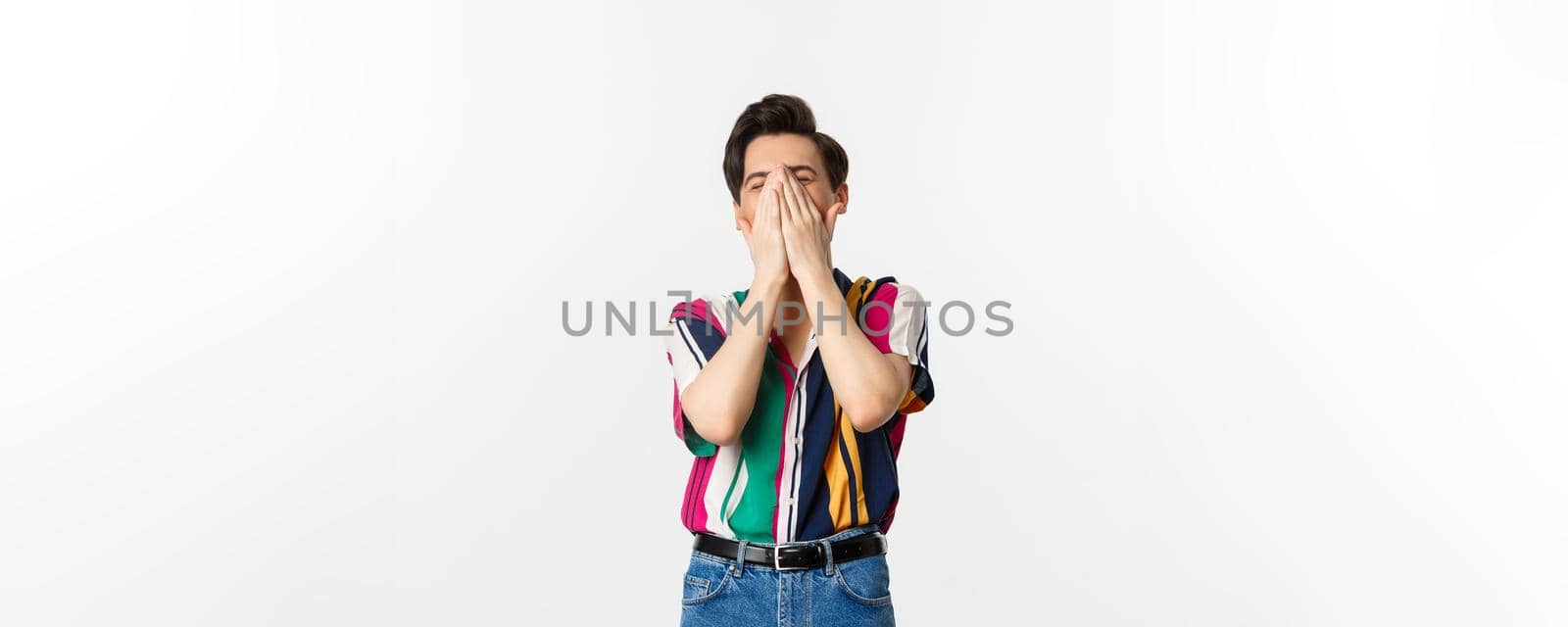 Image of young stylish man sneezing in hands, standing over white background.