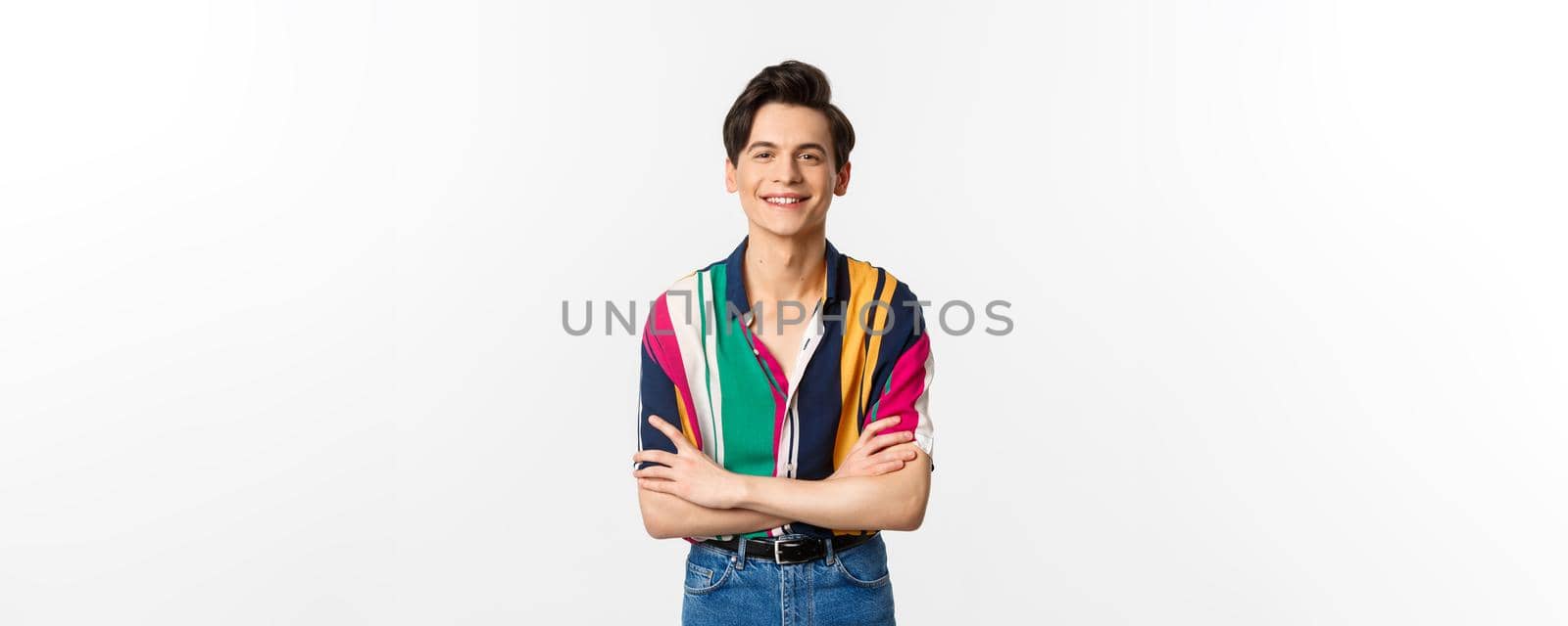 Hansome smiling gay man looking happy, standing over white background in summer outfit.