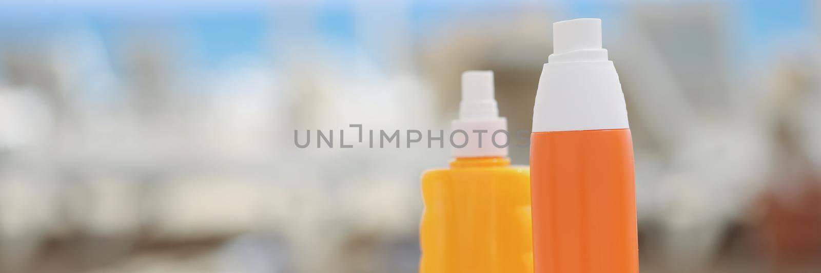 Orange plastic bottles and a beige towel on a beach lounger, close-up, blurry. Cosmetics for sunbathing and relaxation at sea