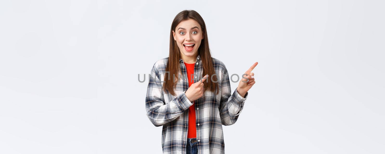 Lifestyle, different emotions, leisure activities concept. Excited girl in checked casual shirt gladly tell about great dicounts, pointing fingers upper right corner, talking to you, rejoicing.