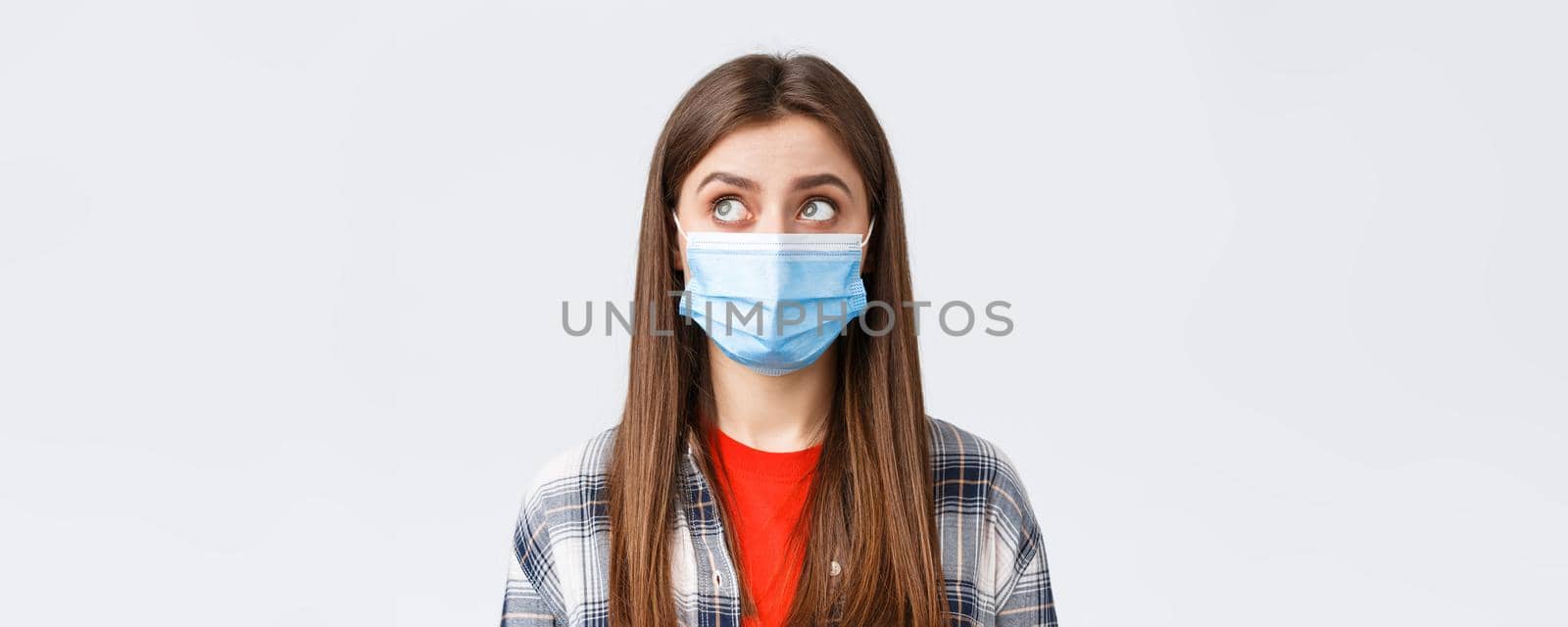 Coronavirus outbreak, leisure on quarantine, social distancing and emotions concept. Close-up of thoughtful, young woman in medical mask, look upper left corner reading sign or have bubble thought.