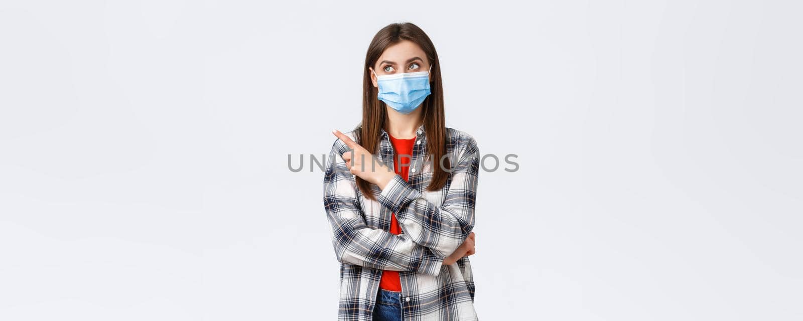 Coronavirus outbreak, leisure on quarantine, social distancing and emotions concept. Young pretty girl in medical mask staying home, search job freelance, pointing finger upper left corner pleased.