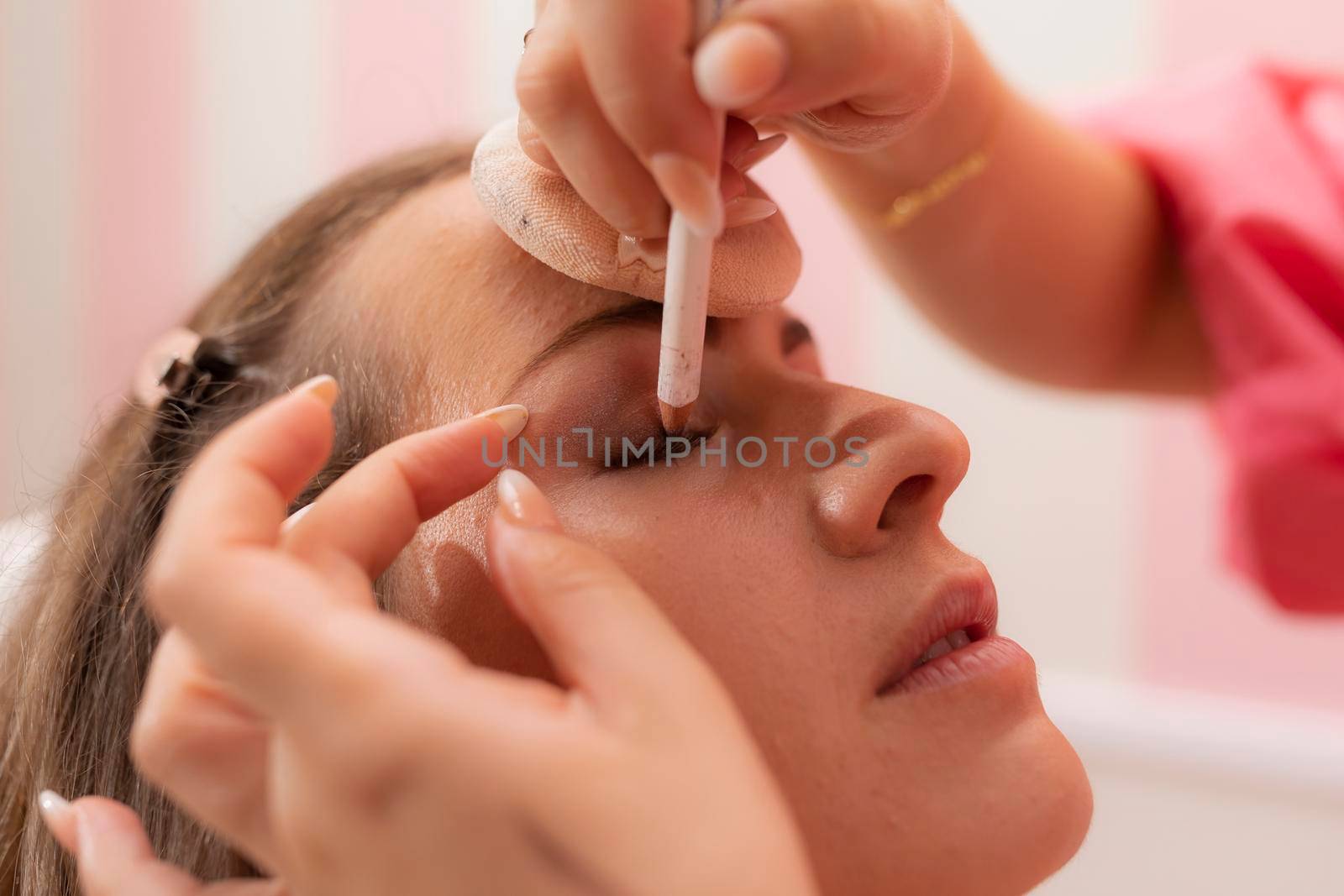 A beautician woman drawing eye shadow on her customer's eyelid during a makeup session at the beauty salon
