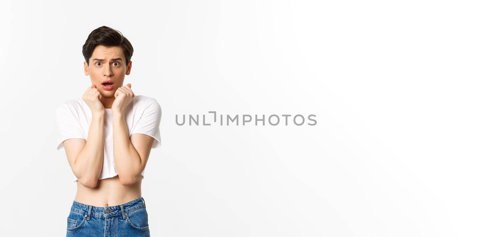 Image of scared androgynous man gasping and looking frightened, staring at something scary, standing in crop top against white background by Benzoix