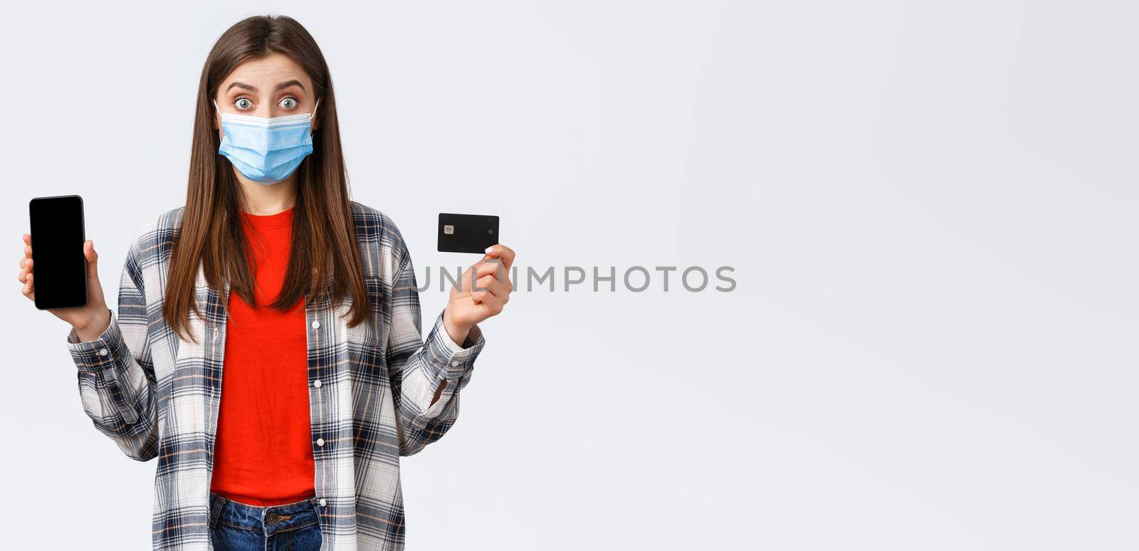 Coronavirus outbreak, working from home, online shopping and contactless payment concept. Excited woman in medical mask showing credit card and mobile phone, look surprised by Benzoix