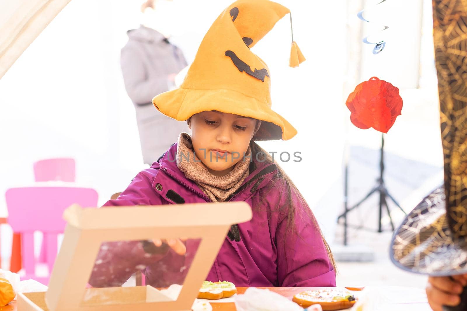 Little kids at a Halloween party. Little girl decorates cookies for Halloween.