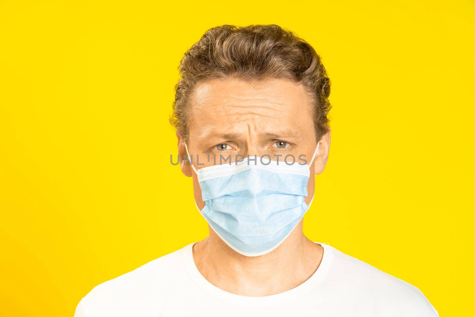 Sad handsome man wearing medical face mask prevention pandemic coronavirus or monkeypox. Handsome man in white t-shirt and medical mask on yellow background. Panoramic, healthcare concept.