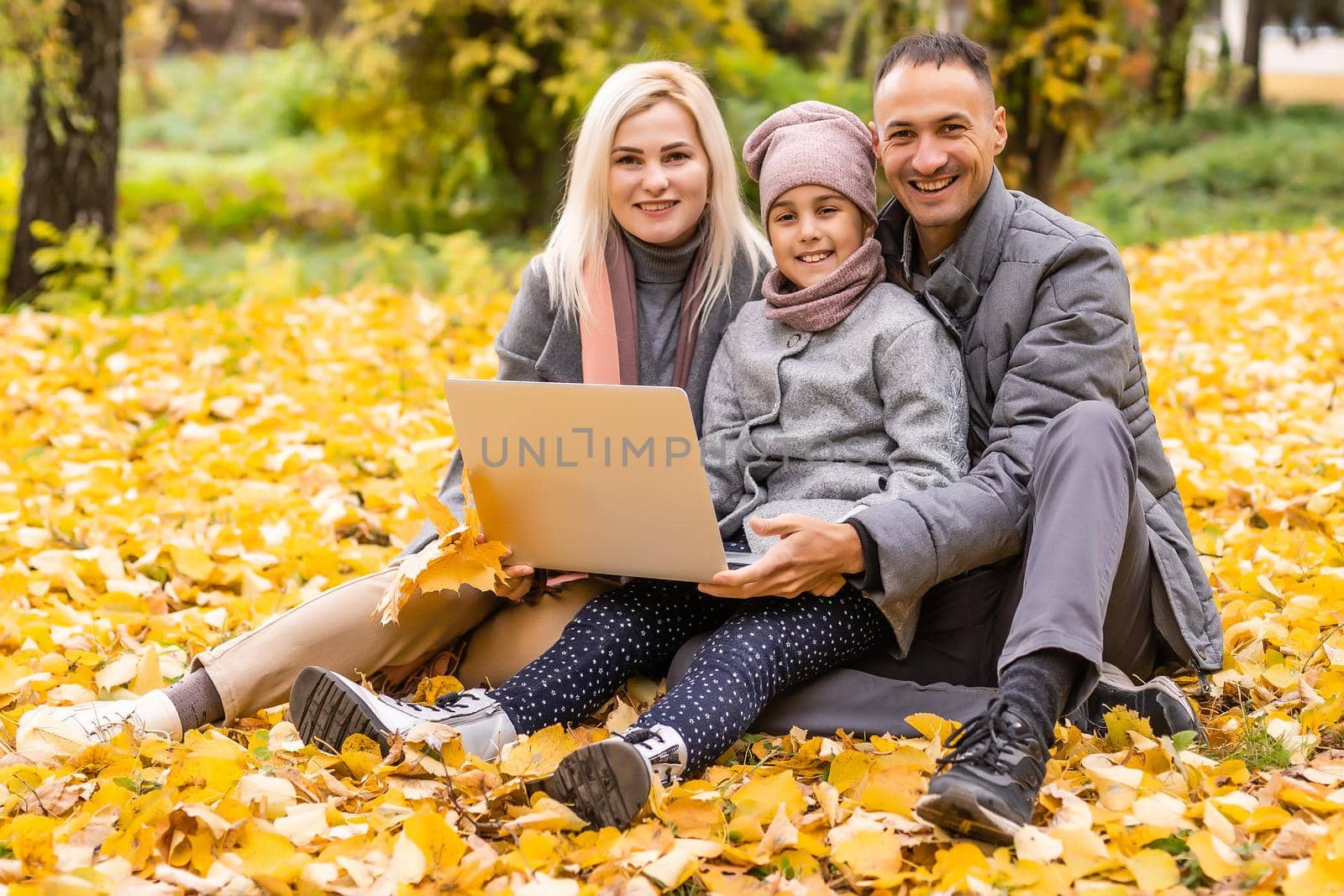 Online communication. Family using laptop and video calling , sitting on picnic blanket in garden. by Andelov13