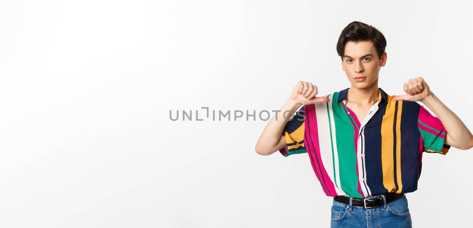 Confident and sassy gay man pointing at himself, looking self-assured, standing over white background.