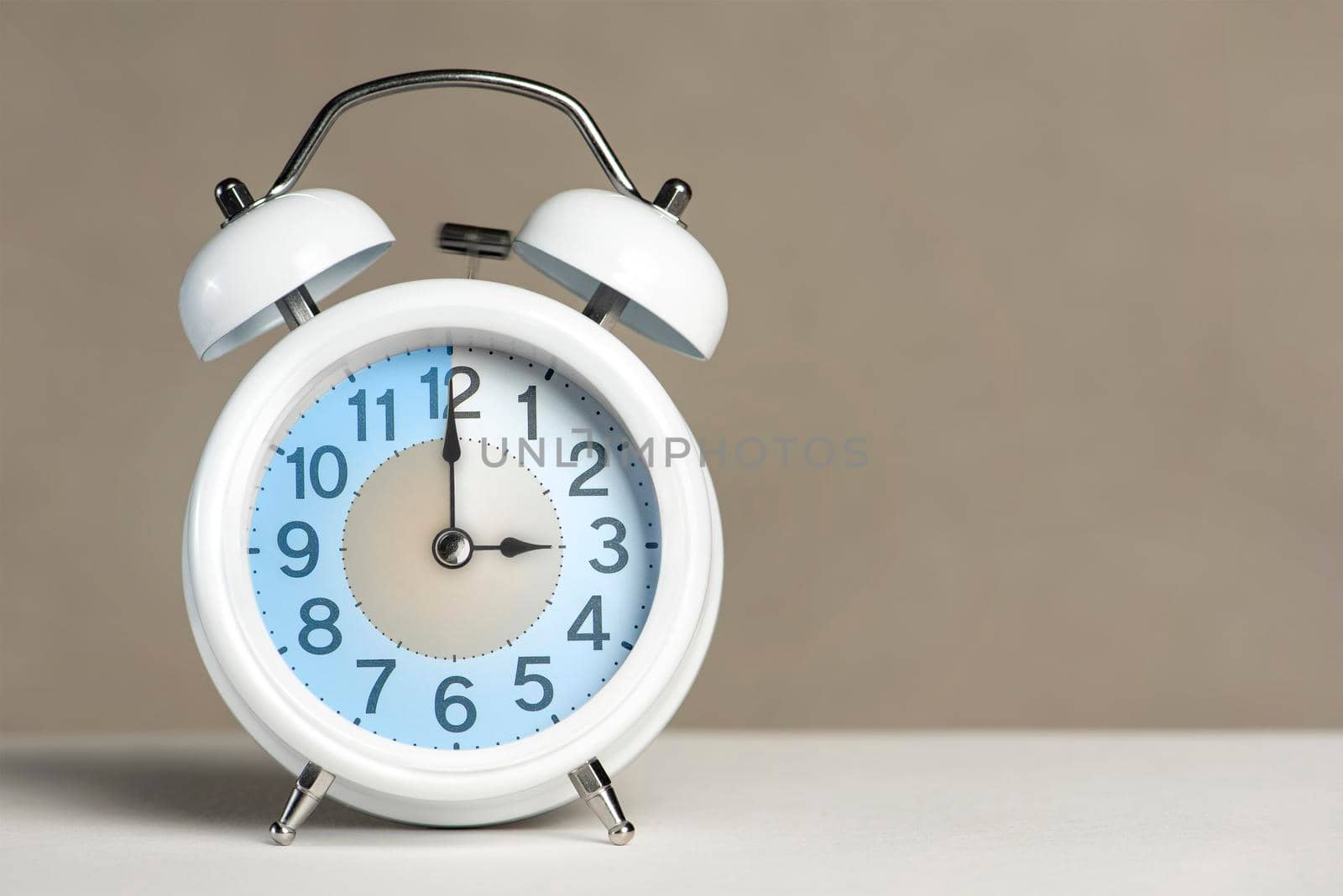 Three hours on the alarm. A white alarm clock is on a white table. The clock hand points to 3 o'clock. Time to change to summer or winter time. Set an alarm for 3:00 or 15:00. copy space.