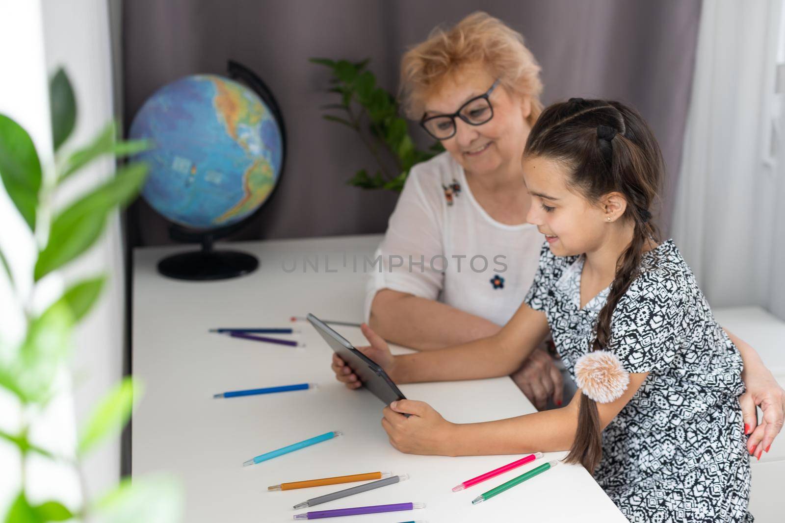 Cute little girl with her grandmother looking at tablet at home.