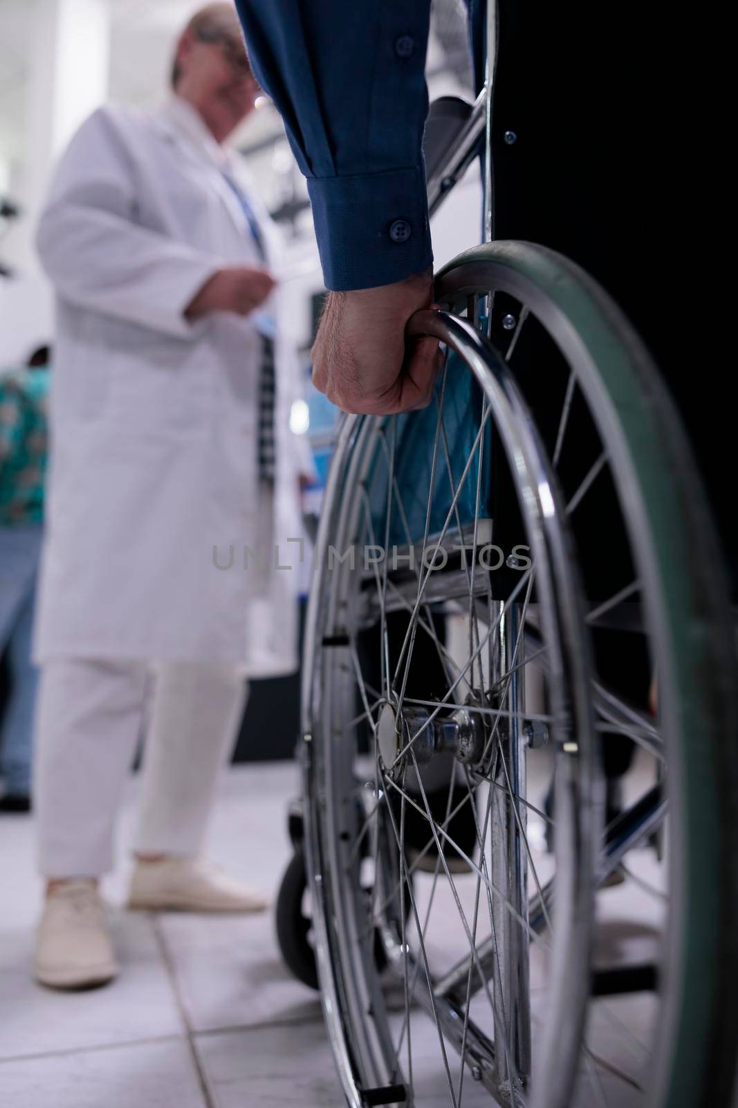 Closeup of older man hand using wheelchair in front of medical doctor for appointment by DCStudio