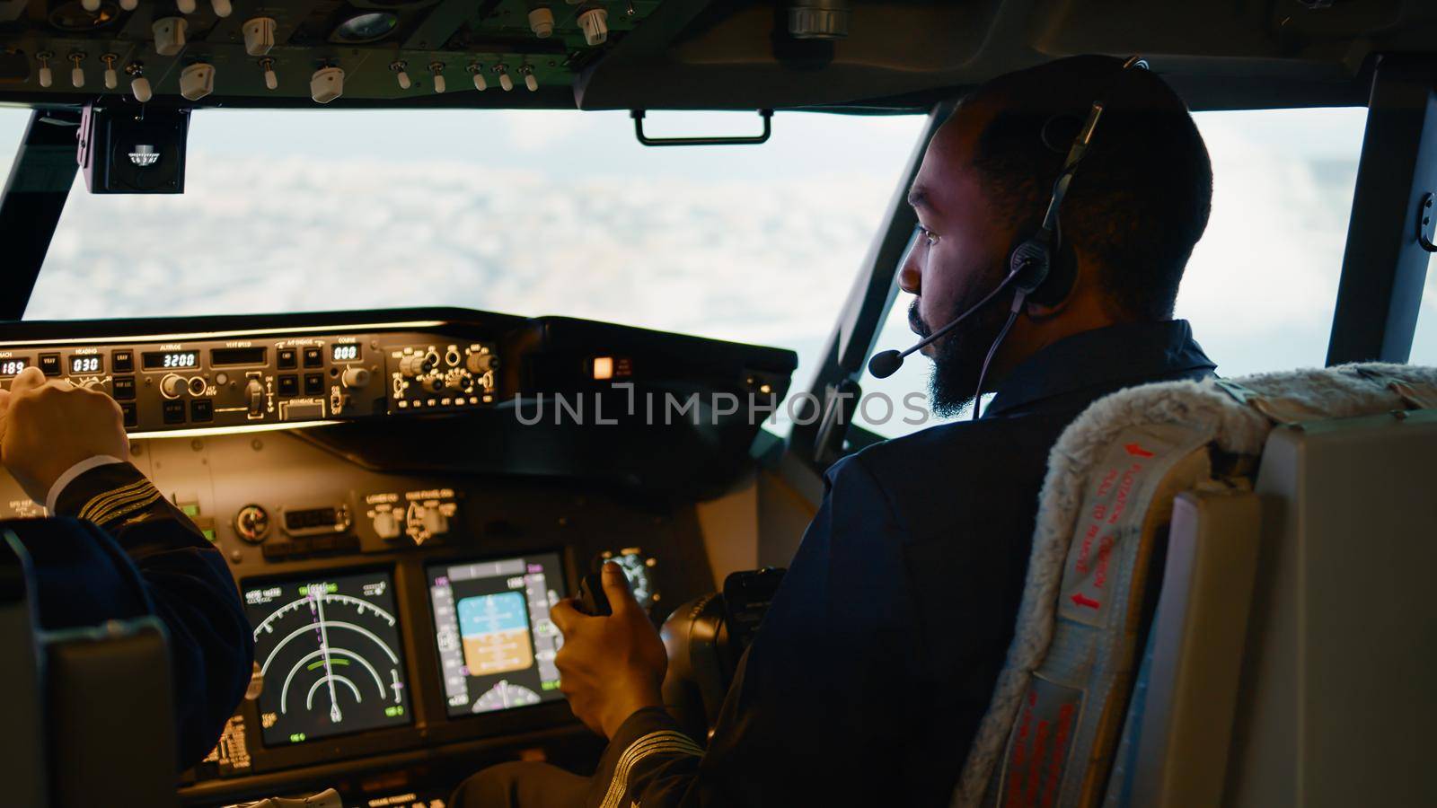 African american copilot flying airplane with captain in cockpit by DCStudio