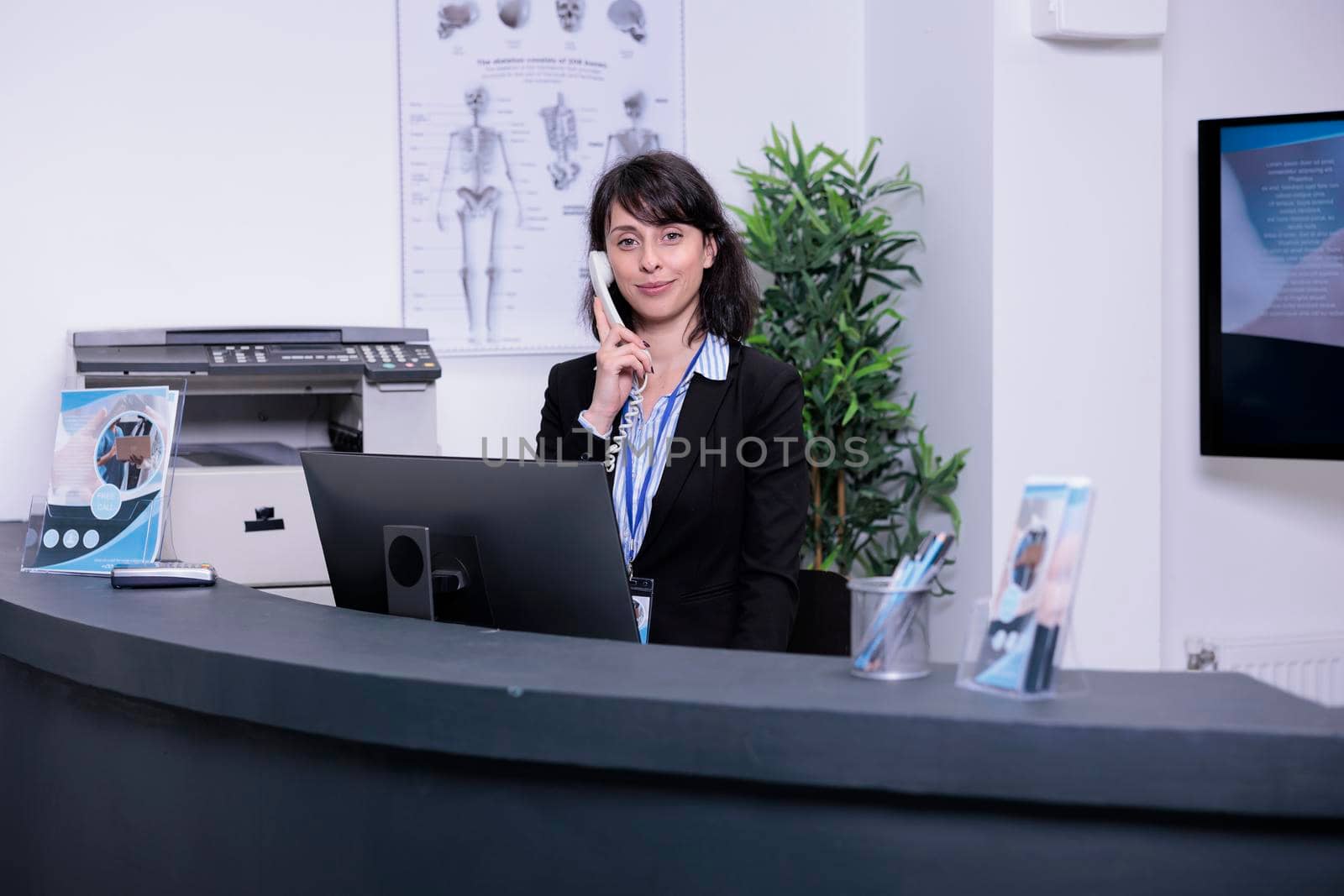 Portrait of smiling hospital receptionist answering call from patient to make an appointment for clinical consult by DCStudio