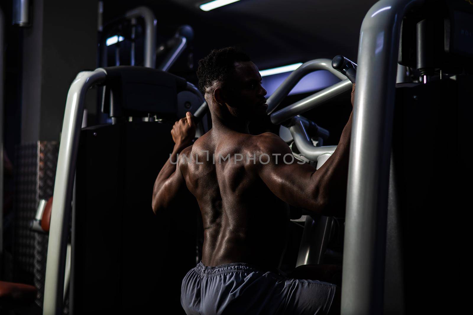 Shirtless african american man doing back exercises on a machine in the gym