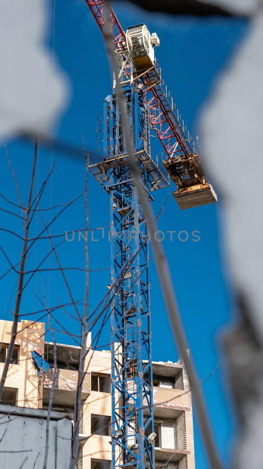 Construction site, crane and the incomplete building with blue sky. New building through an old wall