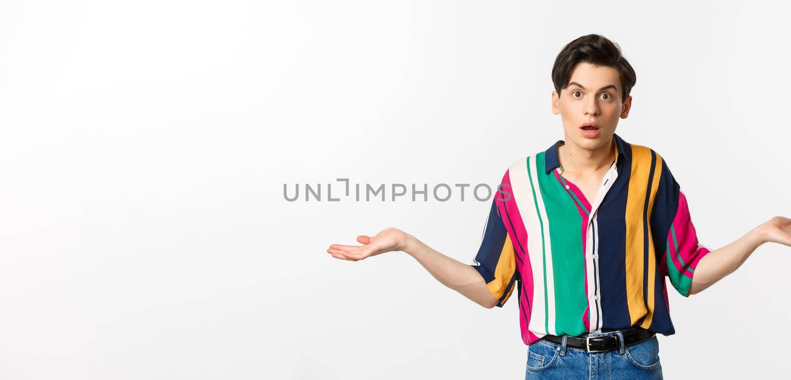 Confused young androgynous man spread hands and looking clueless, dont understand, standing puzzled against white background by Benzoix