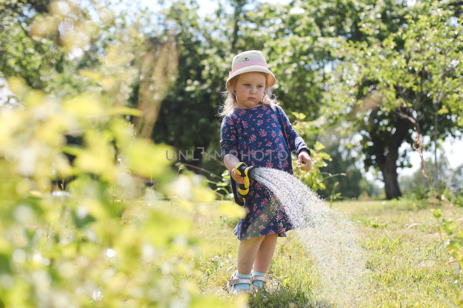 Adorable little girl playing with a garden hose on hot sunny summer day