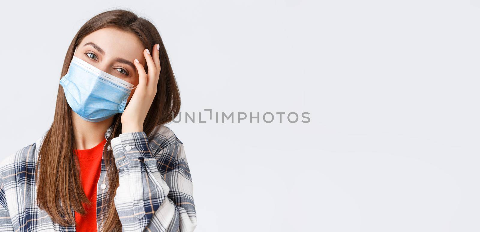 Coronavirus outbreak, leisure on quarantine, social distancing and emotions concept. Close-up of tender happy young woman in medical mask, tilt head, flirting and playing with hair.