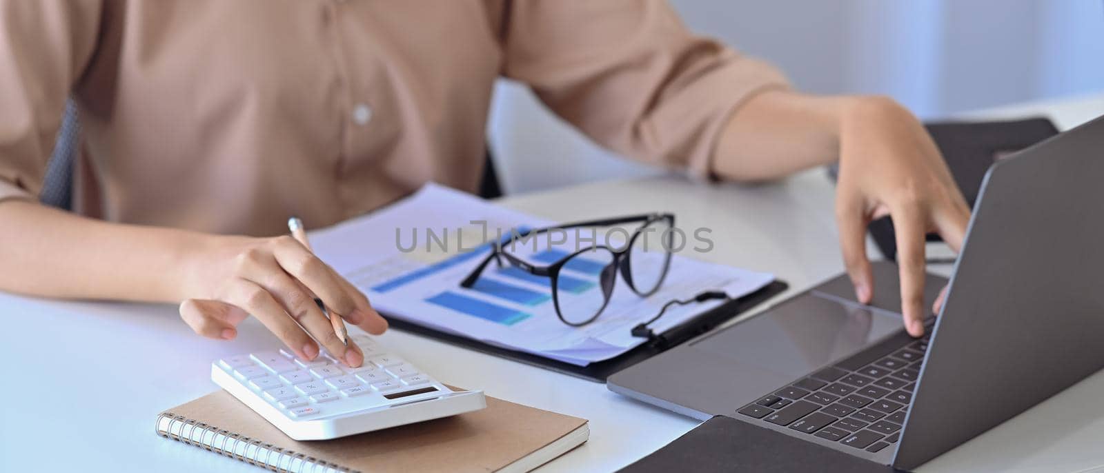 Cropped image of female accountant working with laptop computer and using calculator.