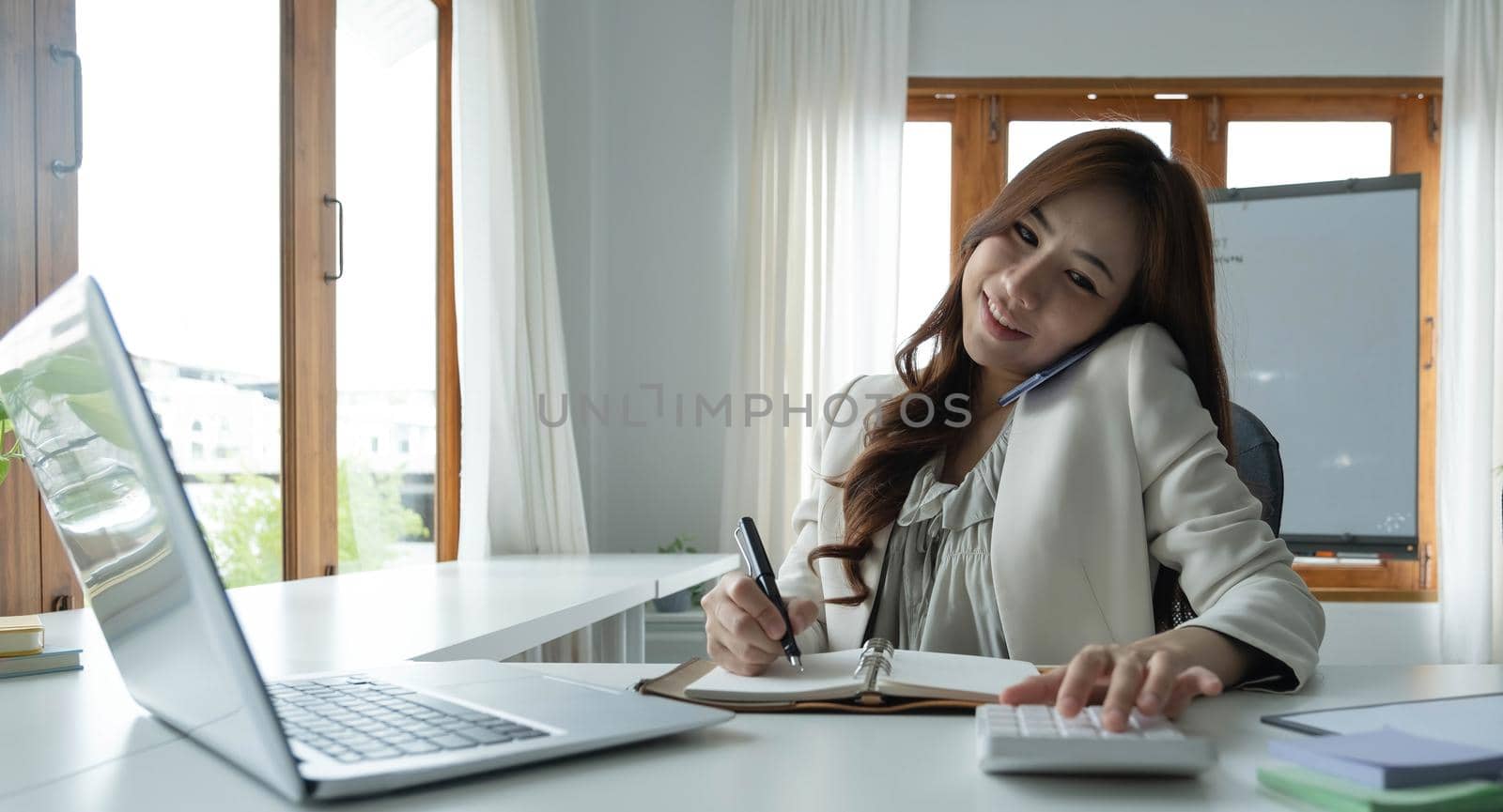 Asian Businesswoman Using laptop computer and working at office with calculator document on desk, doing planning analyzing the financial report, business plan investment, finance analysis concept. by wichayada