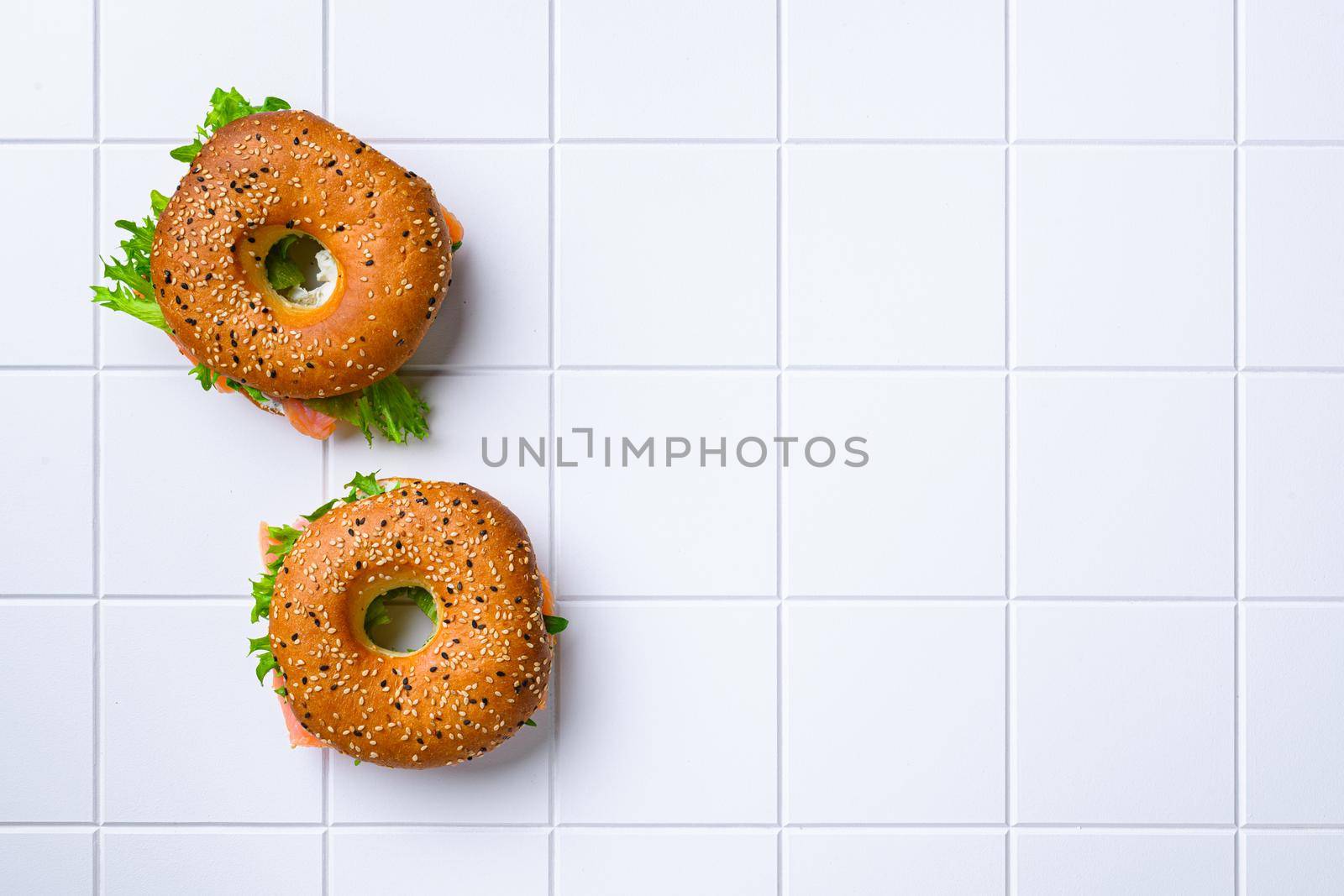 Bagel sandwich with salmon set, on white ceramic squared tile table background, top view flat lay, with copy space for text