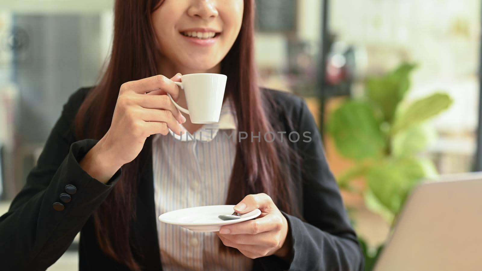 Happy female office worker sitting front of laptop and drinking hot coffee in the morning.