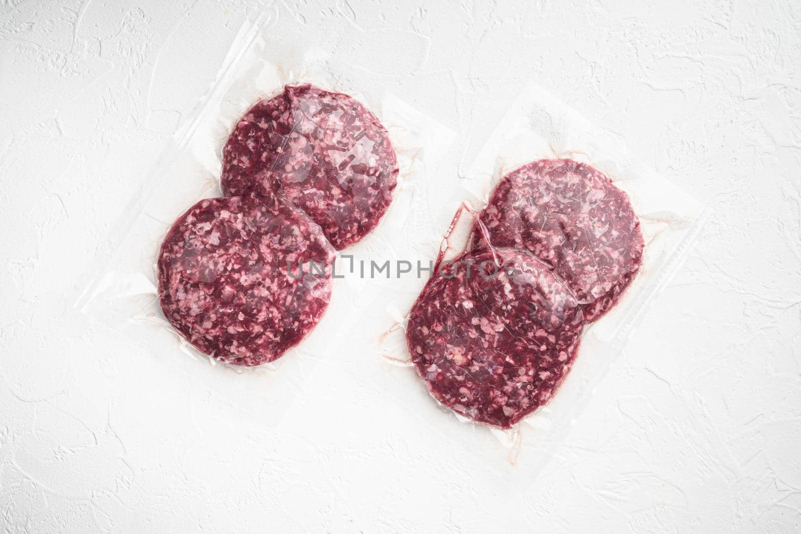 Beef patties in a vacuum packing set, on white stone background, top view flat lay