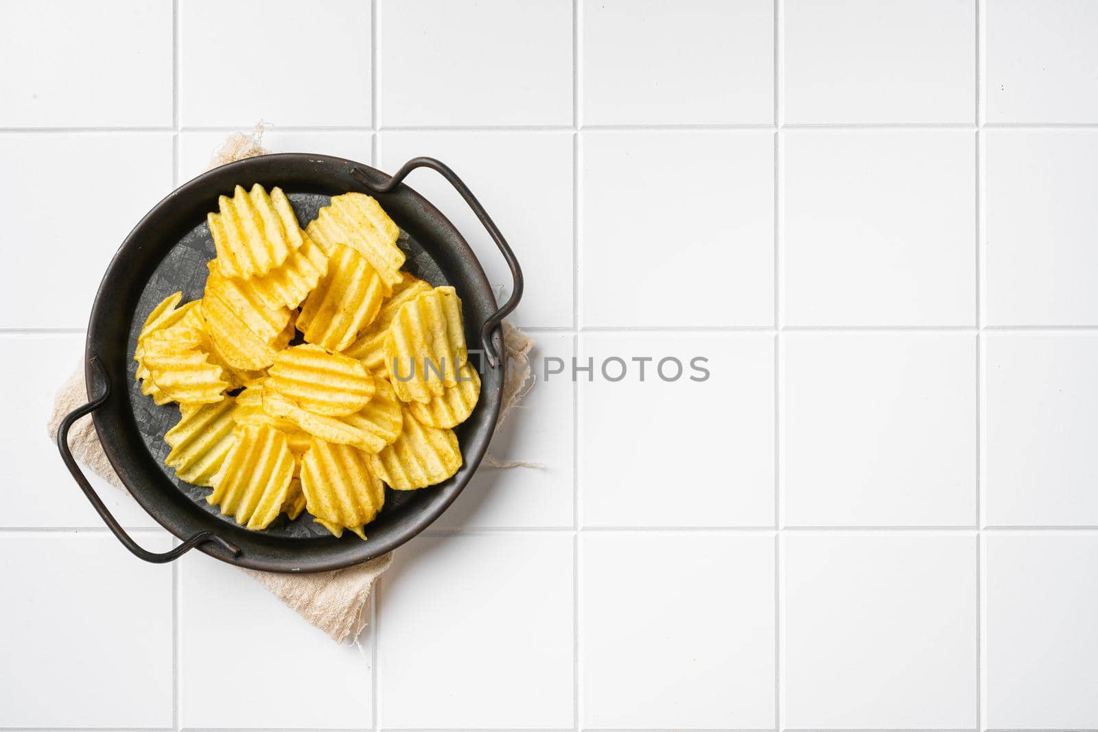Wavy Lightly Salted Potato Chips, on white ceramic squared tile table background, top view flat lay, with copy space for text