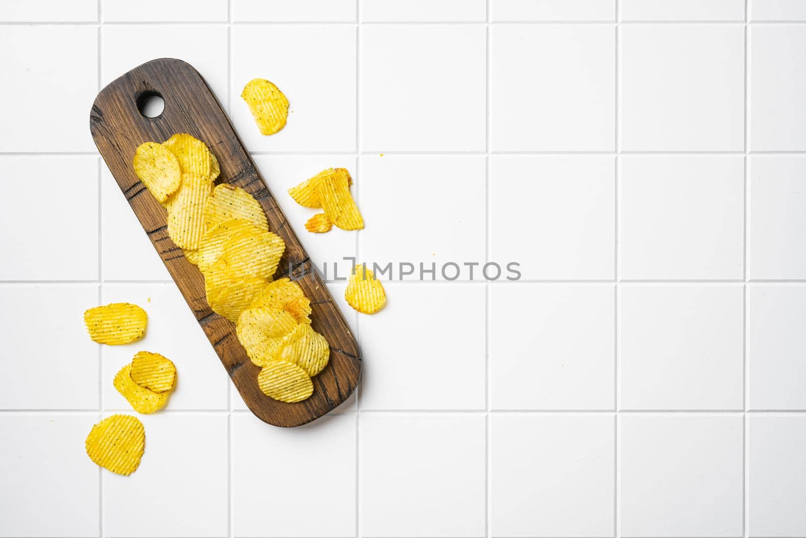 Ridged potato chips, on white ceramic squared tile table background, top view flat lay, with copy space for text