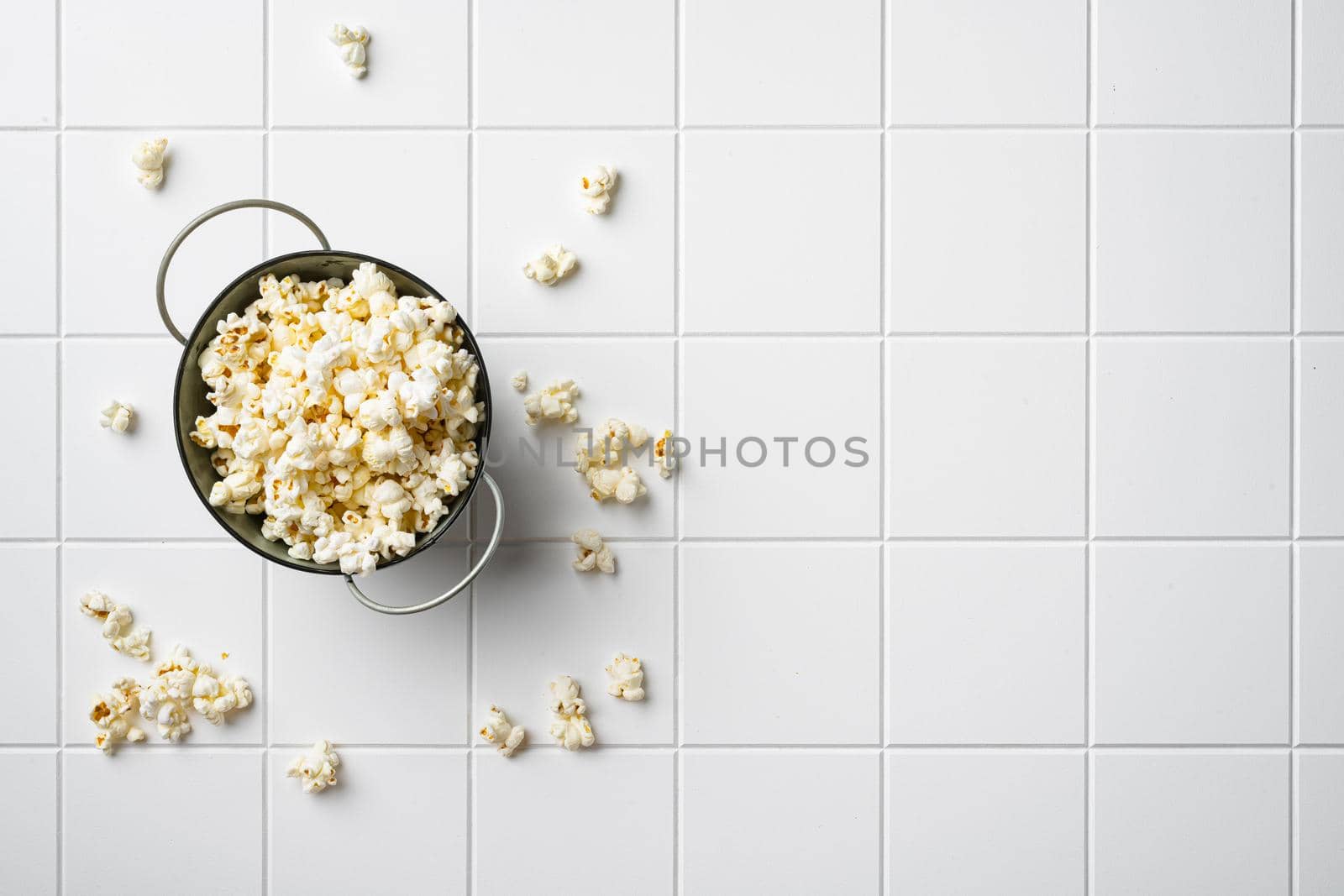 Heap of delicious popcorn on white ceramic squared tile table background, top view flat lay, with copy space for text by Ilianesolenyi