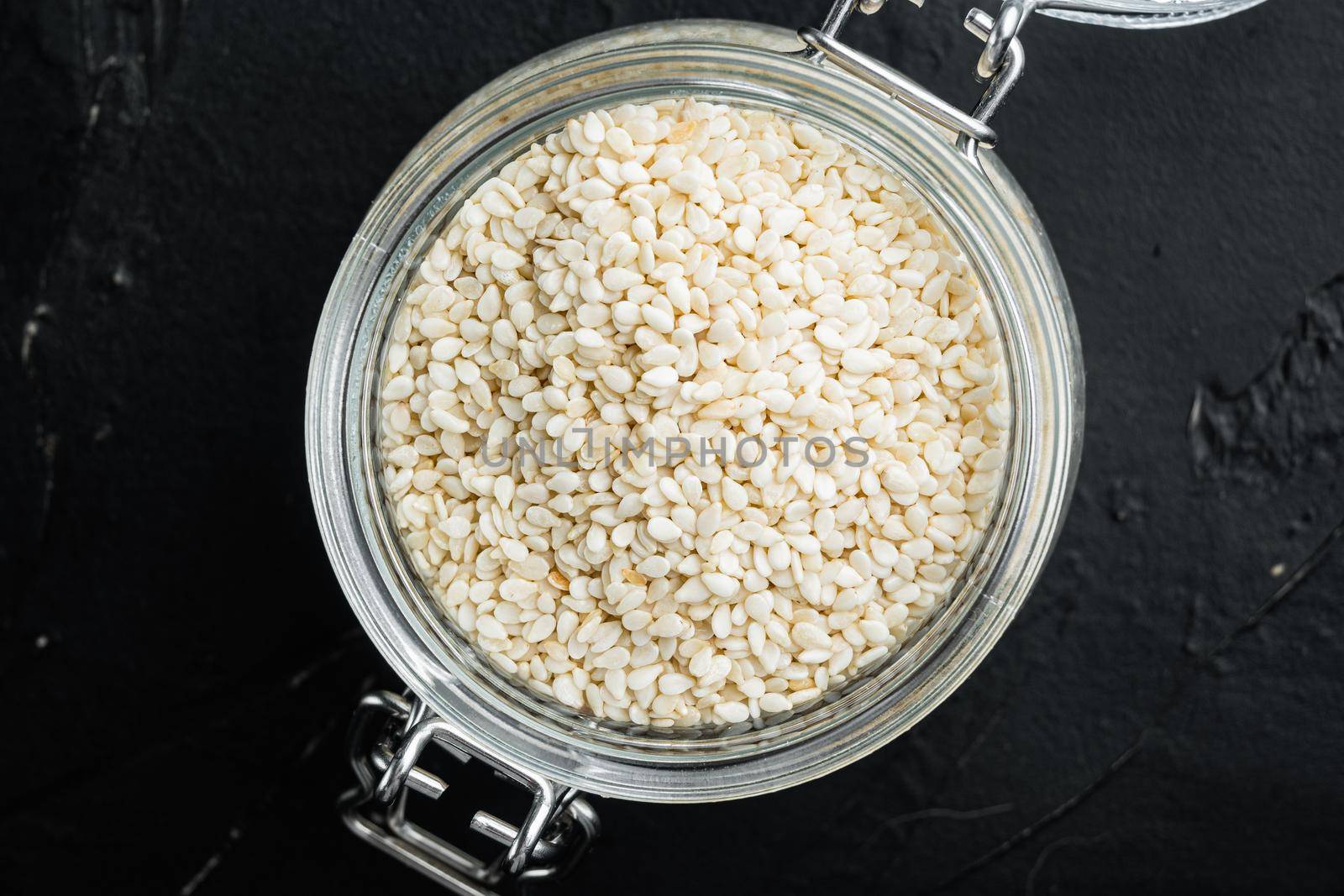 Organic natural sesame seeds set, in glass jar, on black stone background, top view flat lay