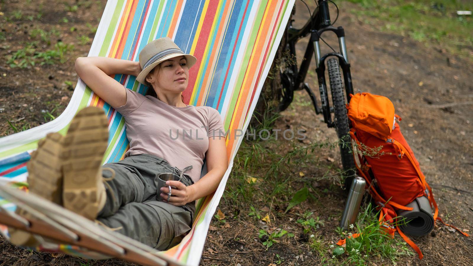 Caucasian woman drinks hot tea from a thermo mug while lying in a hammock in nature. by mrwed54