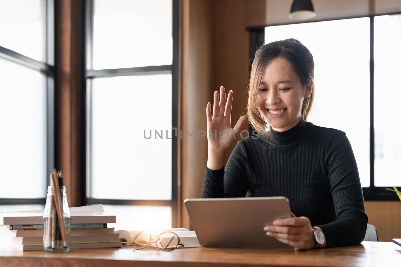 Happy young asian woman waving hand holding digital tablet computer video conference calling by social distance virtual family online chat meeting at home
