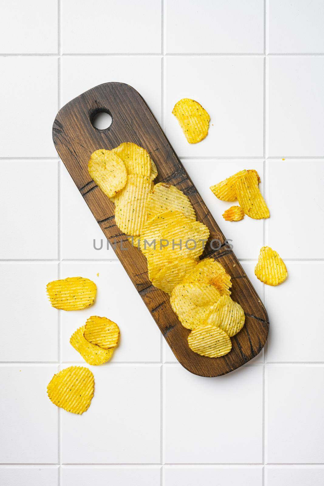 Wavy Potato Chips, on white ceramic squared tile table background, top view flat lay