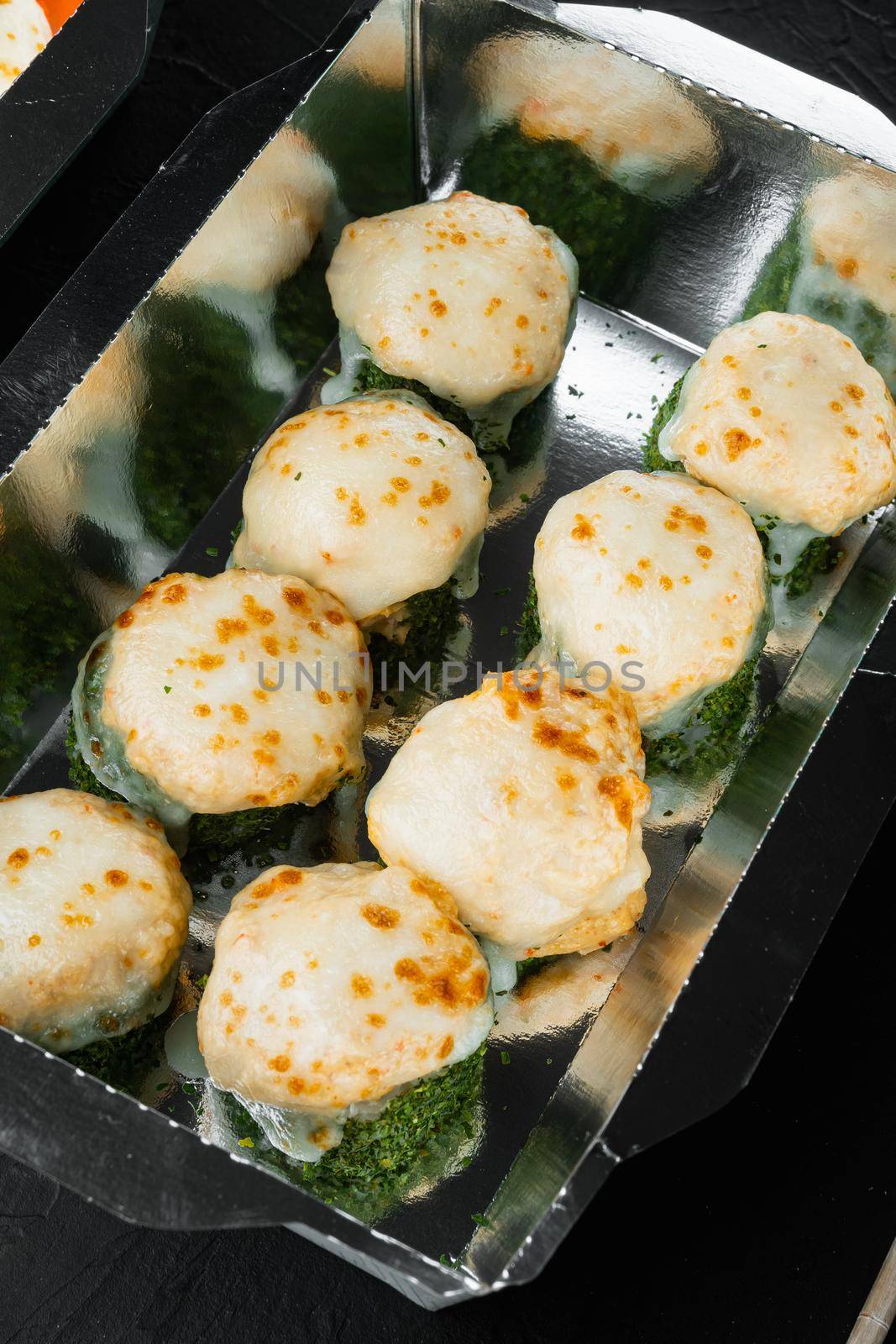 Sushi rolls in takeaway container set, on black stone background