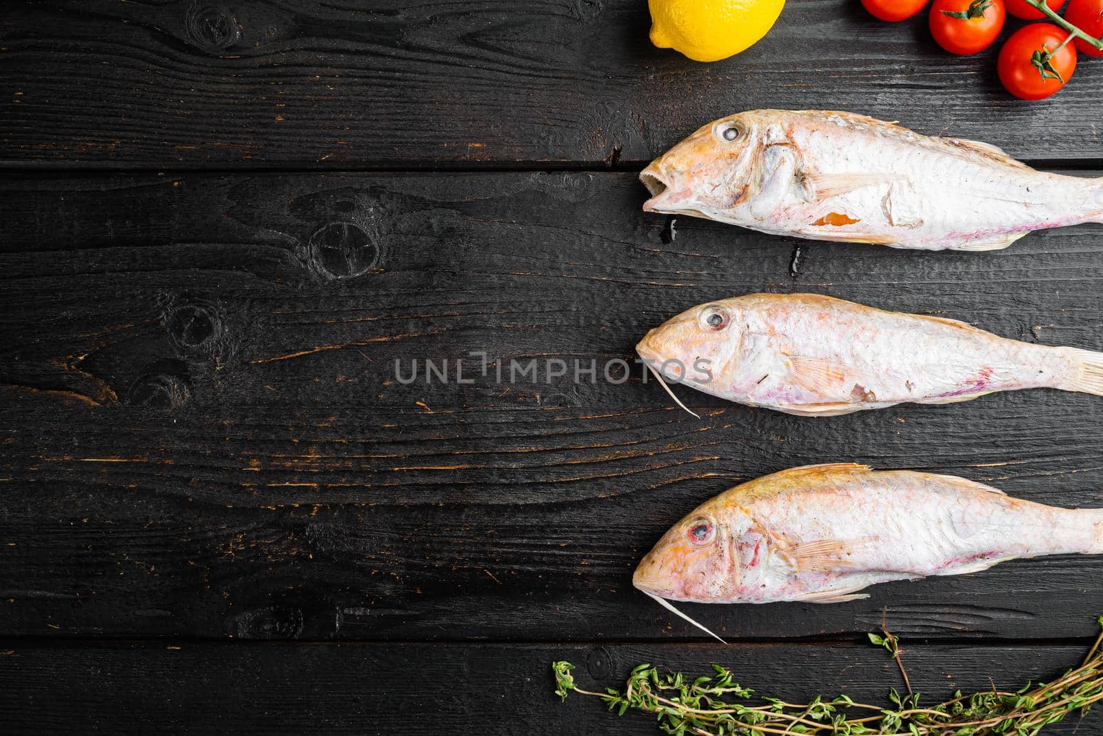 Raw Goatfish fresh whole fish, with ingredients and herbs, on black wooden table background, top view flat lay, with copy space for text by Ilianesolenyi