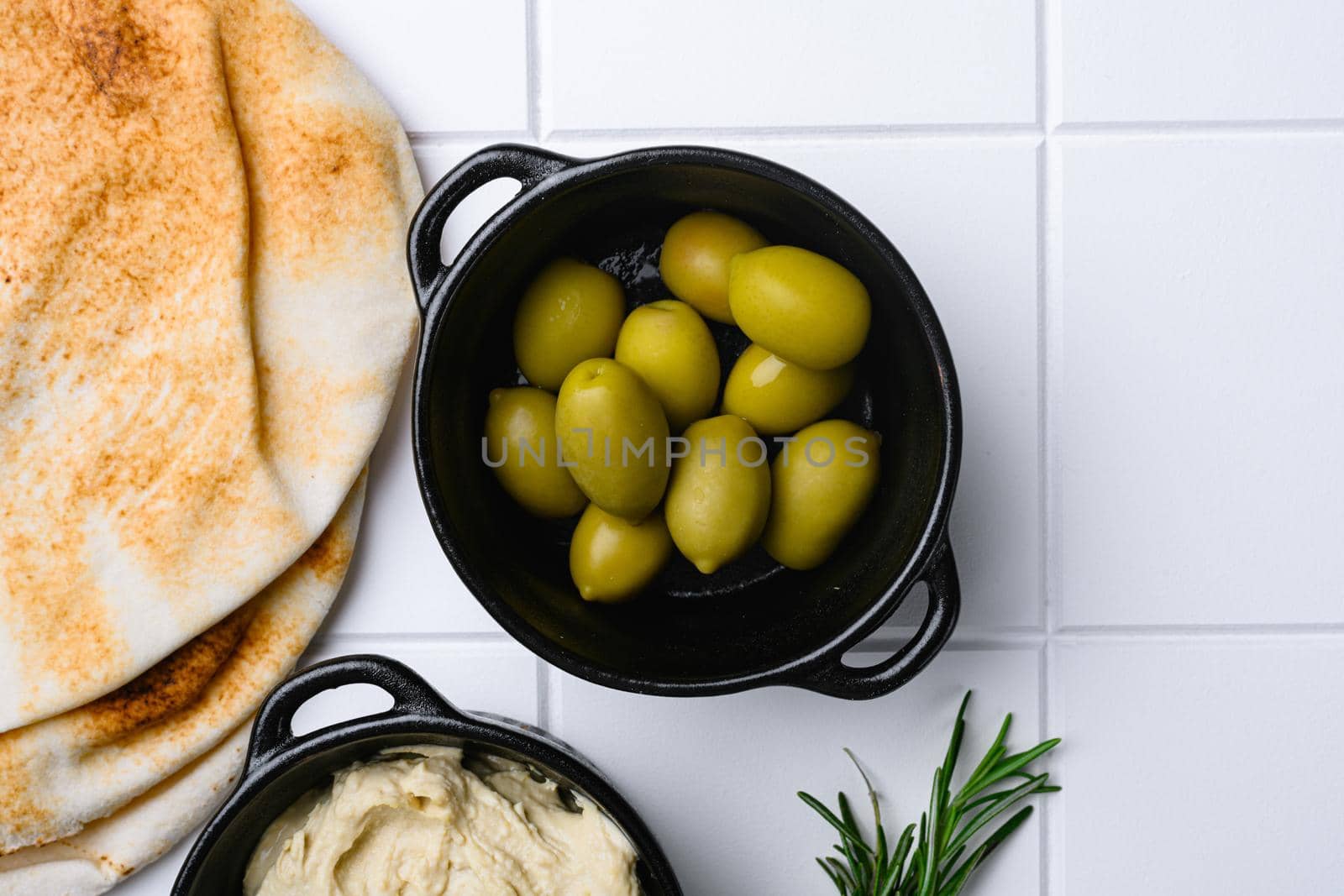 Mediterranean marinated olives set, on white ceramic squared tile table background, top view flat lay, with copy space for text by Ilianesolenyi