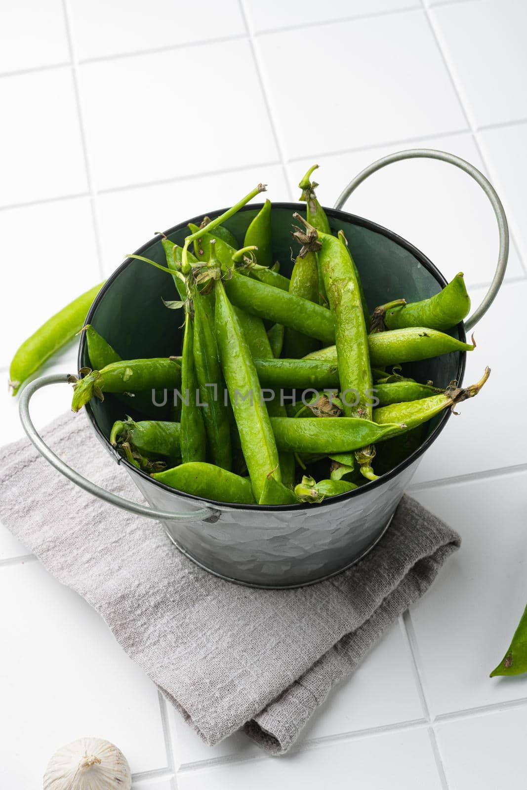 Pods of green peas, on white ceramic squared tile table background