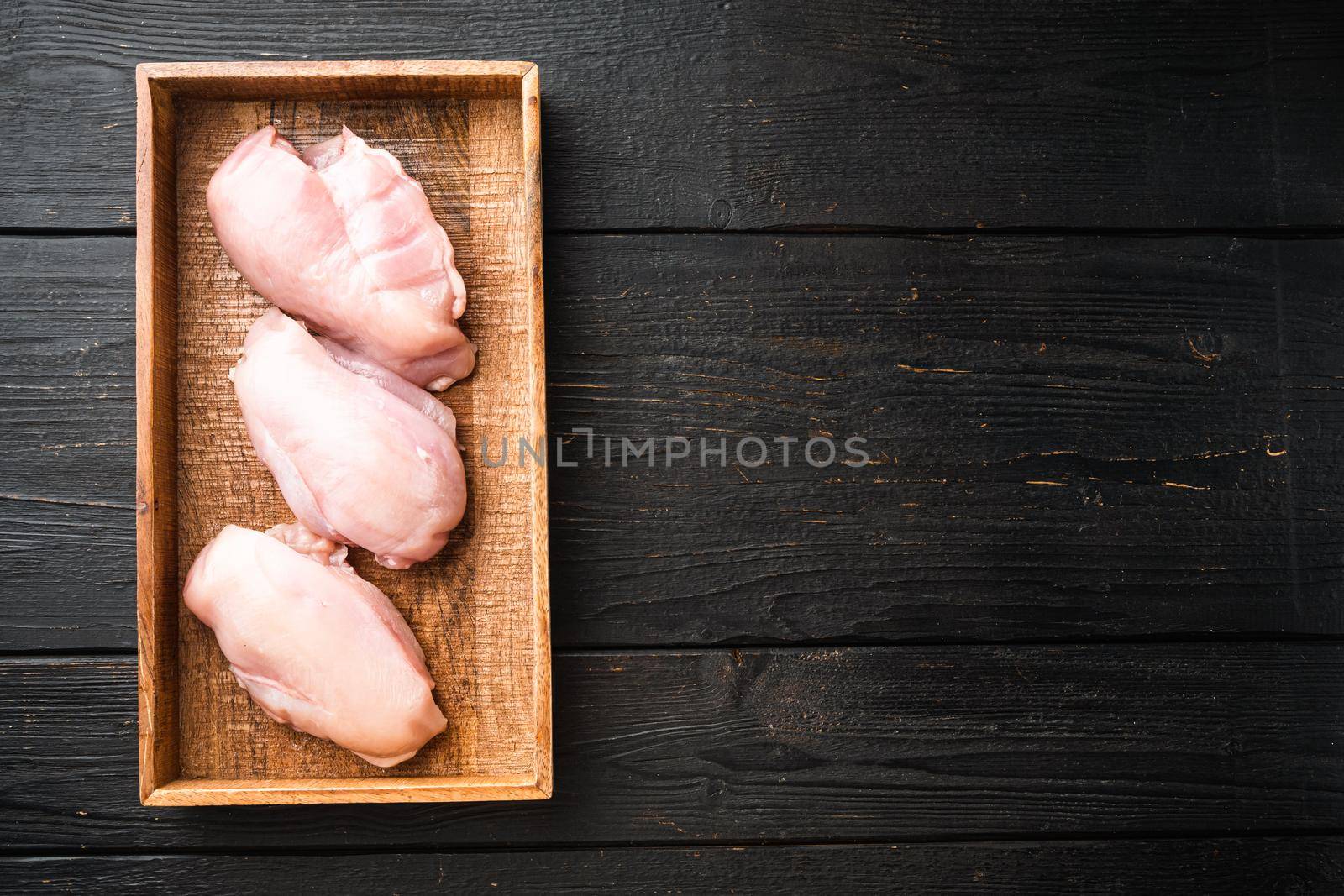 Raw organic chicken Breasts set, in wooden box, on black wooden table background, top view flat lay, with copy space for text