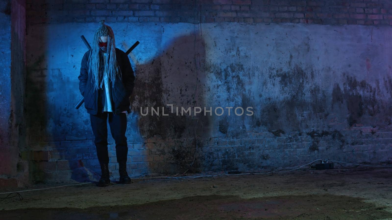 a girl with dreadlocks and katanas in red glasses is texting on a mobile phone against a neon brick wall 4k